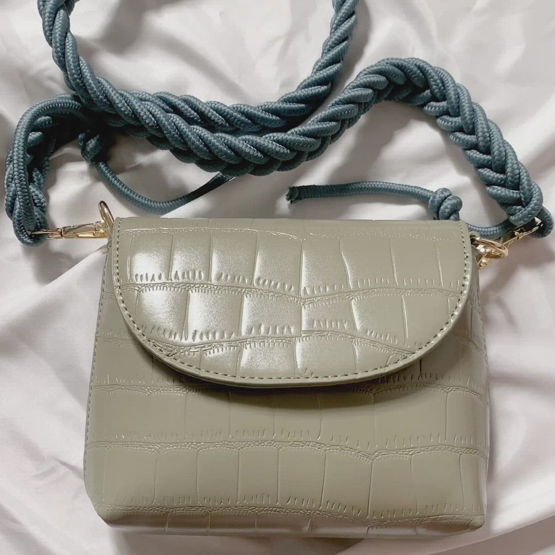 A rectangular crossbody flap bag with pleated straps. 