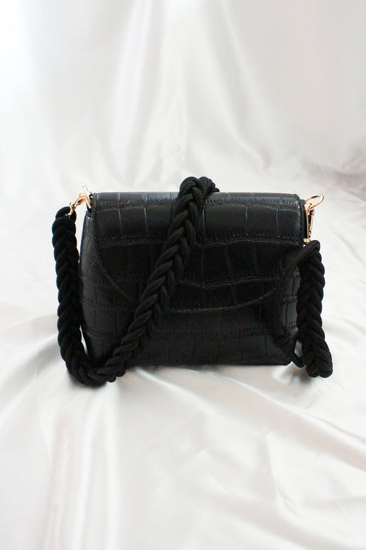 A black rectangular crossbody flap bag with pleated straps. 