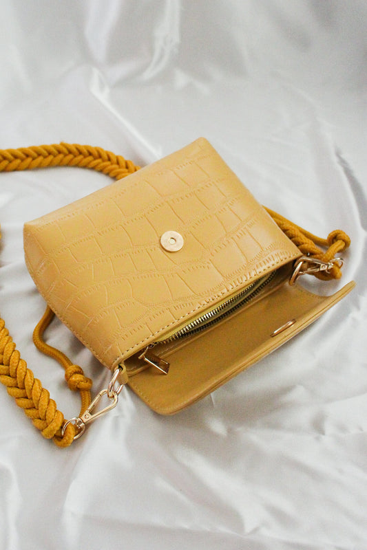 A mustard yellow rectangular crossbody flap bag with pleated straps. 
